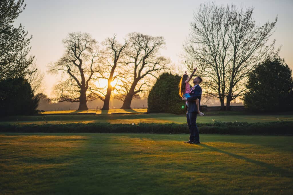 Groom lifting daughter at wedding against beautiful sunset