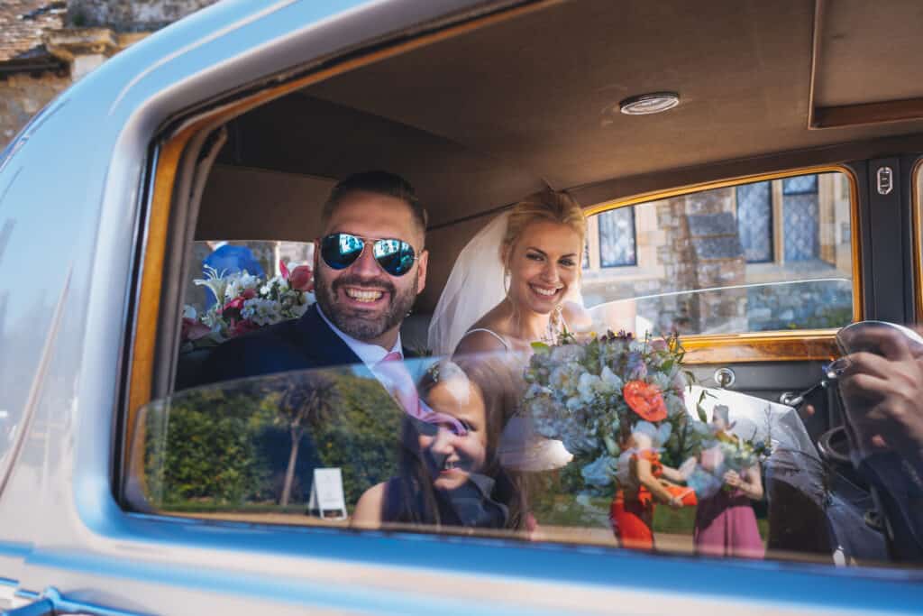 Bride and groom in wedding car with flower girl reflection in window